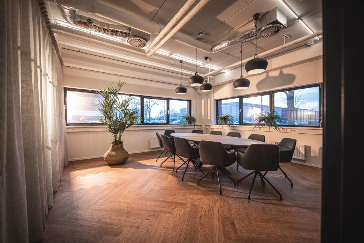 Vergaderruimte Wolga met een grote ovale tafel, omringd door stoelen en omgeven door planten en grote ramen.