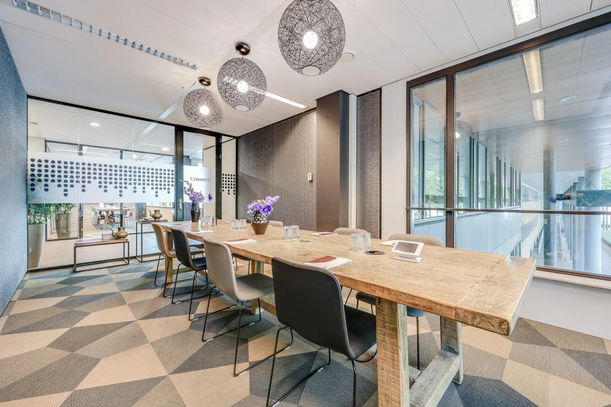 Vergaderruimte in Tribes Amsterdam met een lange houten tafel, moderne stoelen en glazen wanden met decoraties.