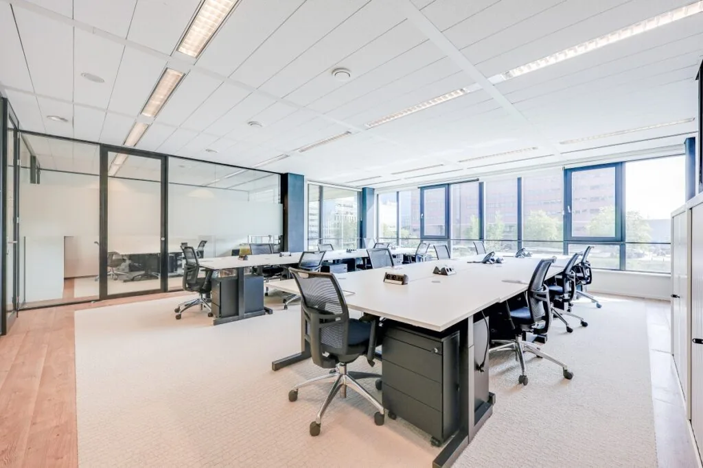 Een moderne, lichte kantoorruimte met werkplekken en uitzicht op een stadsomgeving bij Tribes Amsterdam Adam Smith.