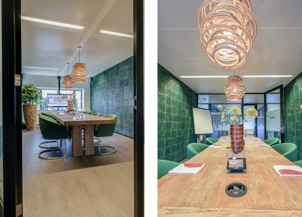 Een moderne vergaderruimte met een houten tafel en groene stoelen bij Tribes Amsterdam Amstel.