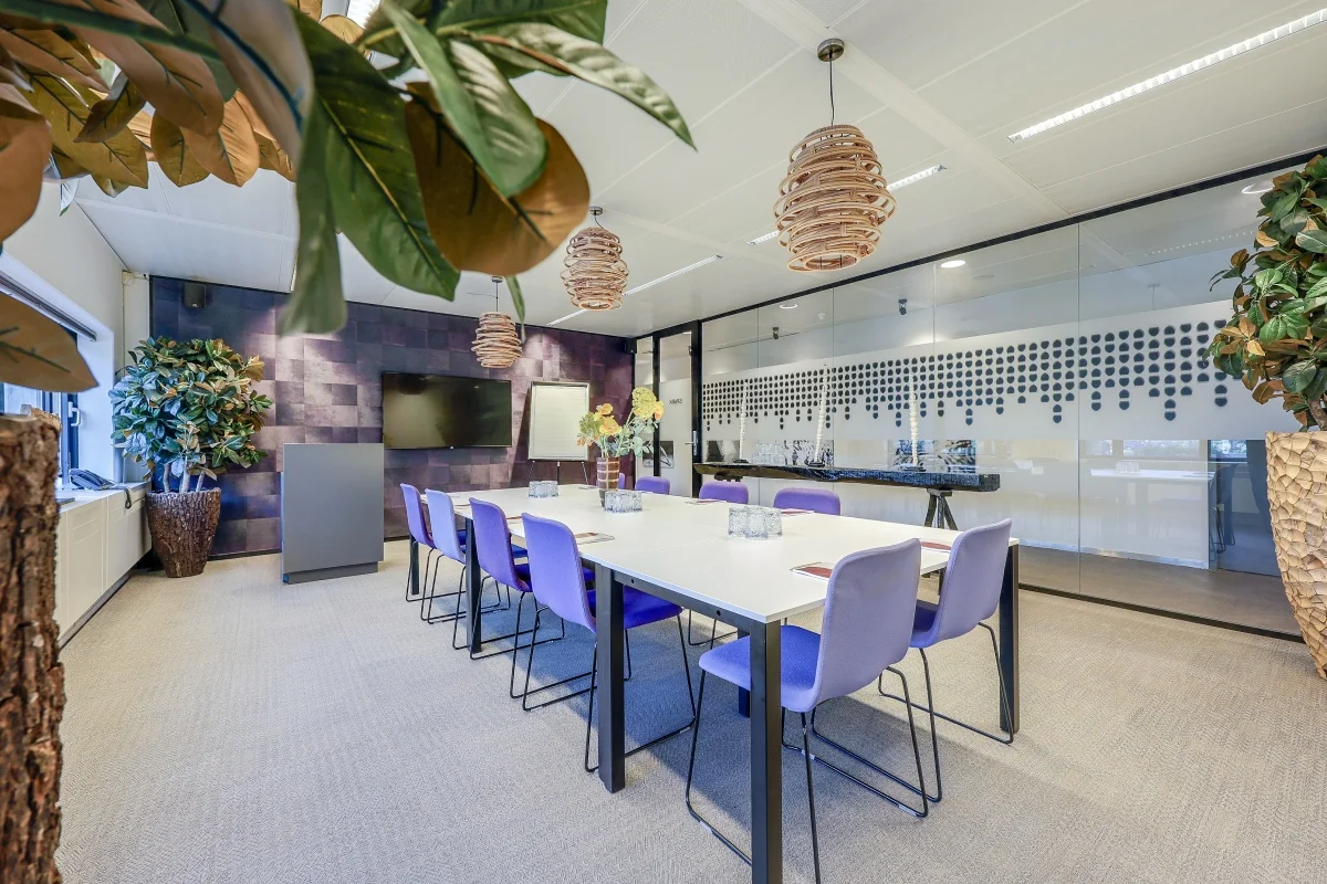 Vergaderruimte met een lange tafel, paarse stoelen, planten en moderne verlichting in Tribes Amsterdam Amstel.