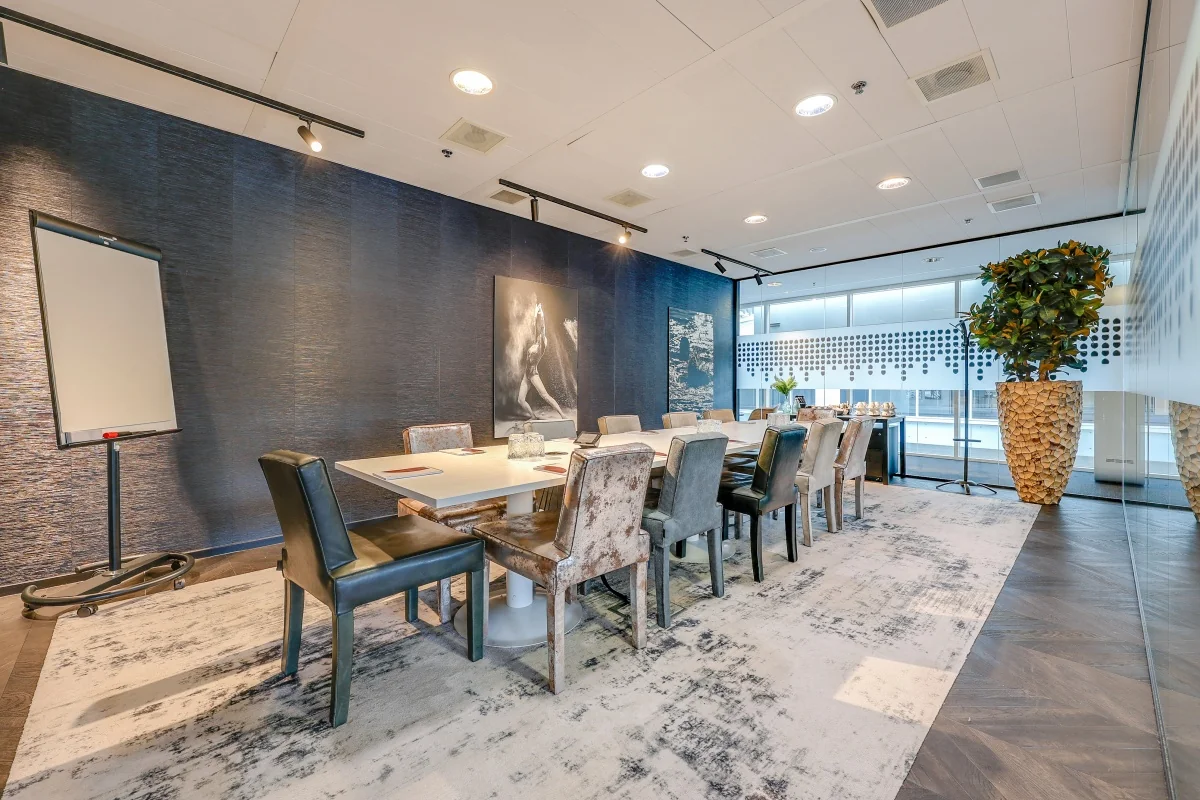 Vergaderruimte bij Tribes Amsterdam South Axis ITO met een lange tafel, stijlvolle stoelen, blauwe wanddecoratie en grote planten.