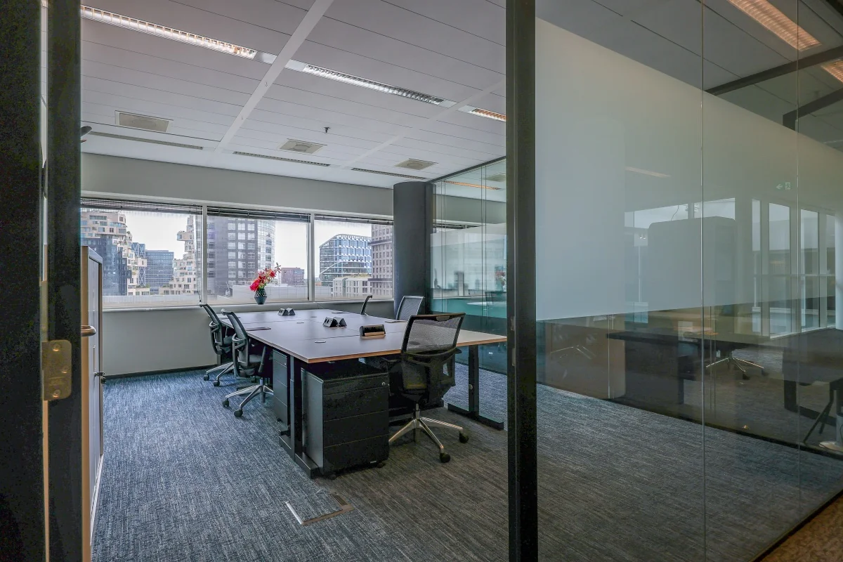 Een moderne privé-kantoorruimte met een grote vergadertafel en stoelen, omgeven door glazen wanden, in Tribes Amsterdam South Axis ITO.
