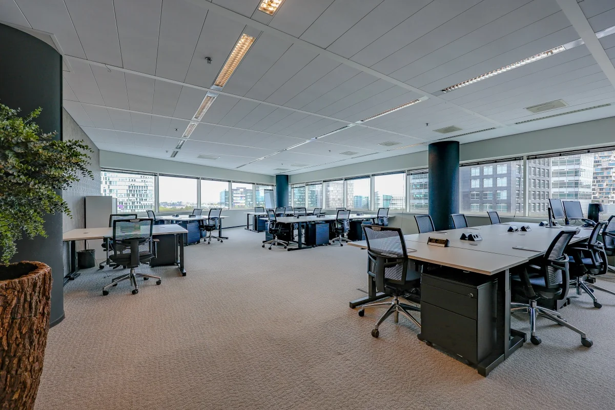 Een moderne kantoorruimte met grote ramen, bureaus en ergonomische stoelen bij Tribes Amsterdam South Axis.