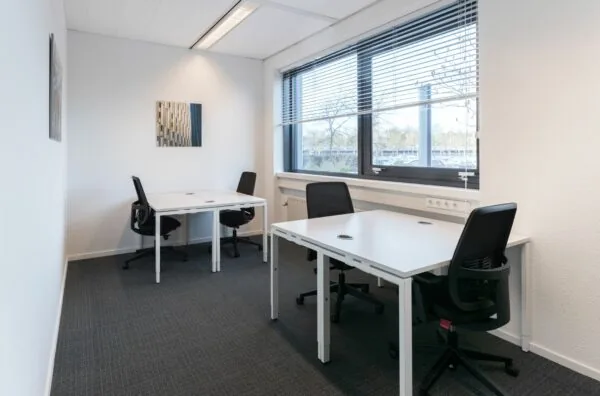 Kleine, lichte kantoorruimte aan de Nevelgaarde 8 met vier werkplekken en een groot raam met uitzicht naar buiten.