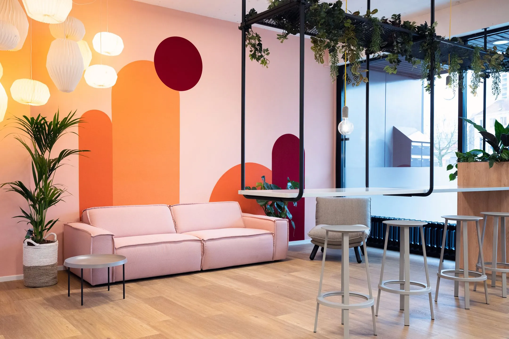 Moderne en kleurrijke zithoek in Newday Arnhem met een zachtroze bank, designverlichting en planten tegen een grafisch beschilderde muur.