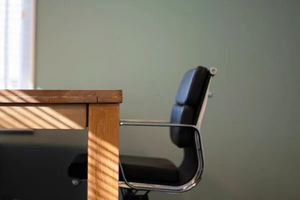 Zwarte bureaustoel en houten tafel in een zonnige ruimte van Office-Hotel Kennemerplein, april 2021.
