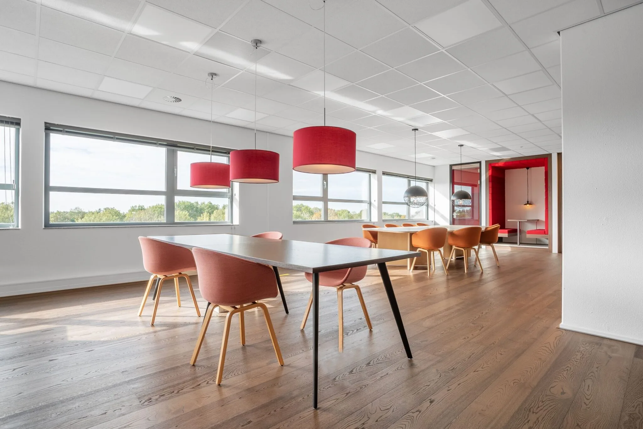 Moderne kantoorruimte aan de Papendorpseweg 75 met grote ramen, houten vloer, kleurrijke stoelen en hanglampen.