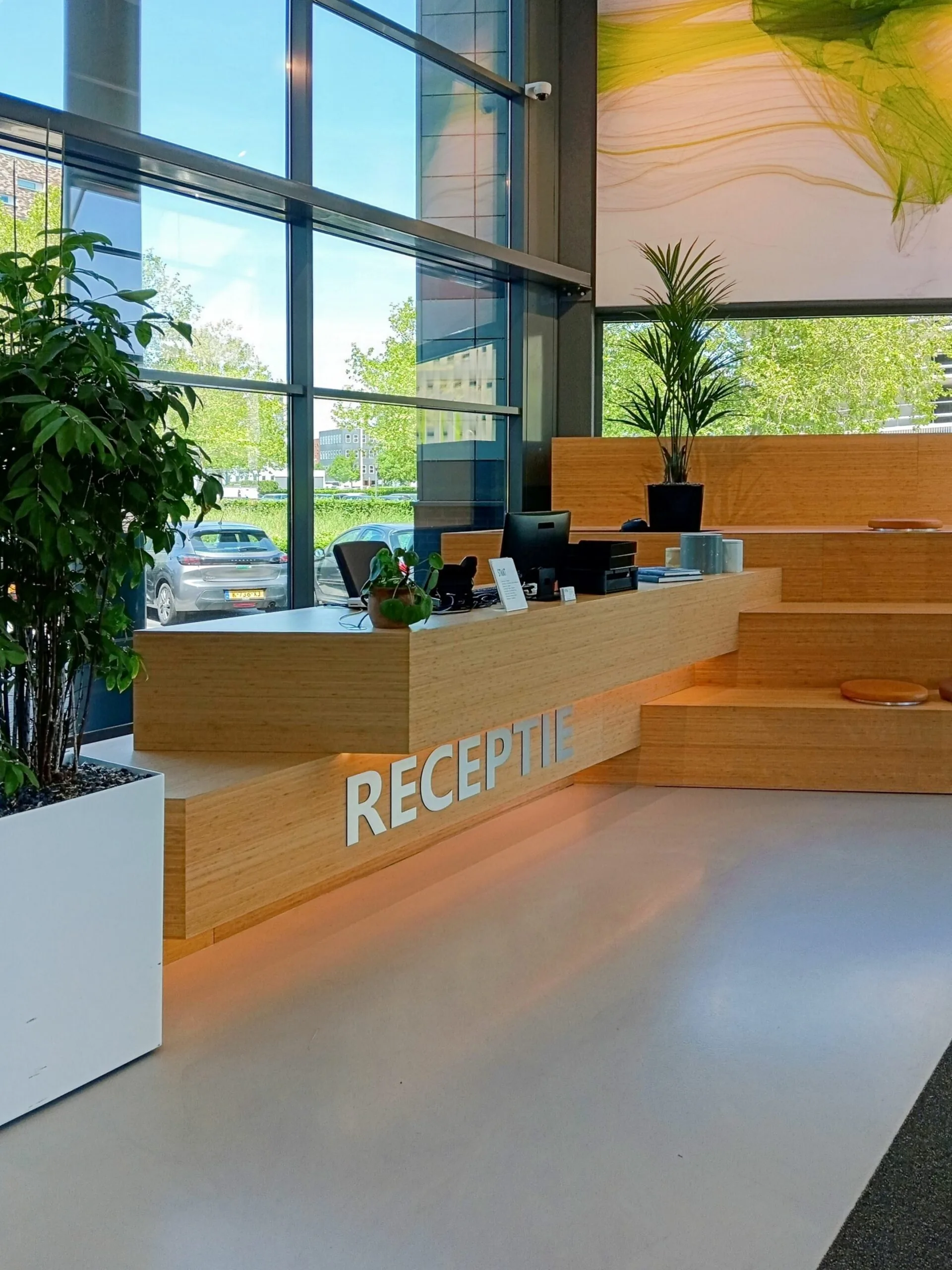 Moderne receptiebalie van hout met planten en grote ramen aan de Papendorpseweg 75.