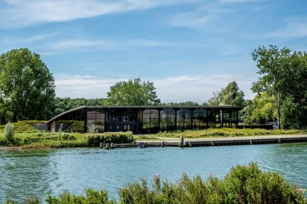 Modern gebouw aan het water met grote glazen gevel bij Plaatweg 15, omringd door groen.