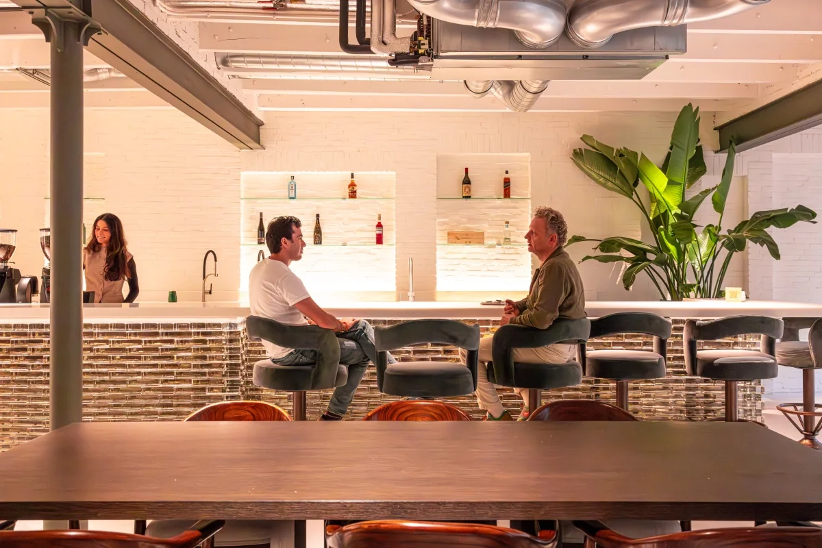 Twee mannen zitten aan een moderne bar terwijl een vrouw achter de bar staat in een vergaderruimte aan de Keizersgracht.