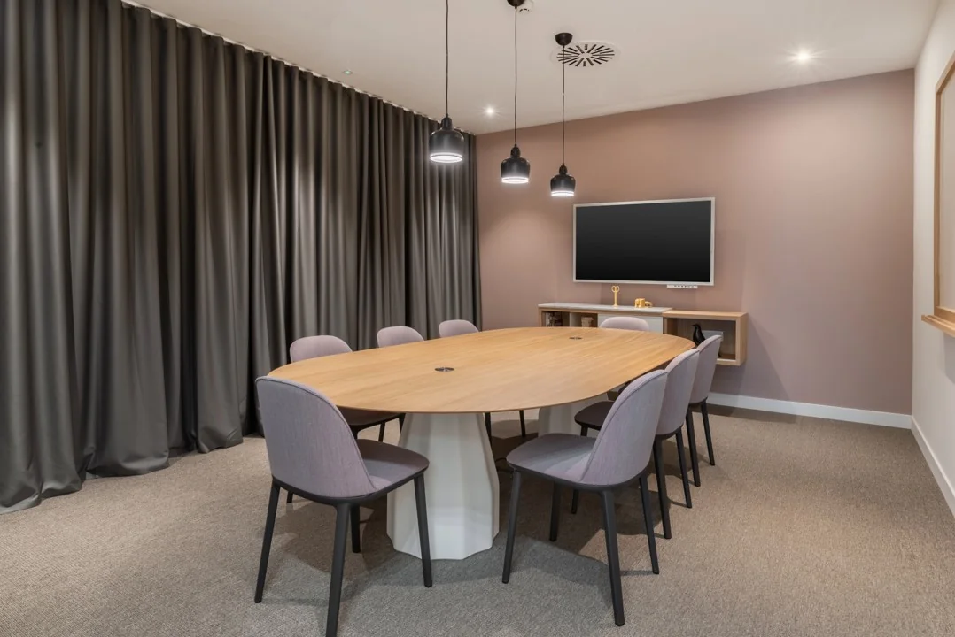 Moderne vergaderruimte aan het Rotterdam Airportplein 22 met ovaal houten tafel, acht stoelen, een flatscreen en sfeervolle verlichting.