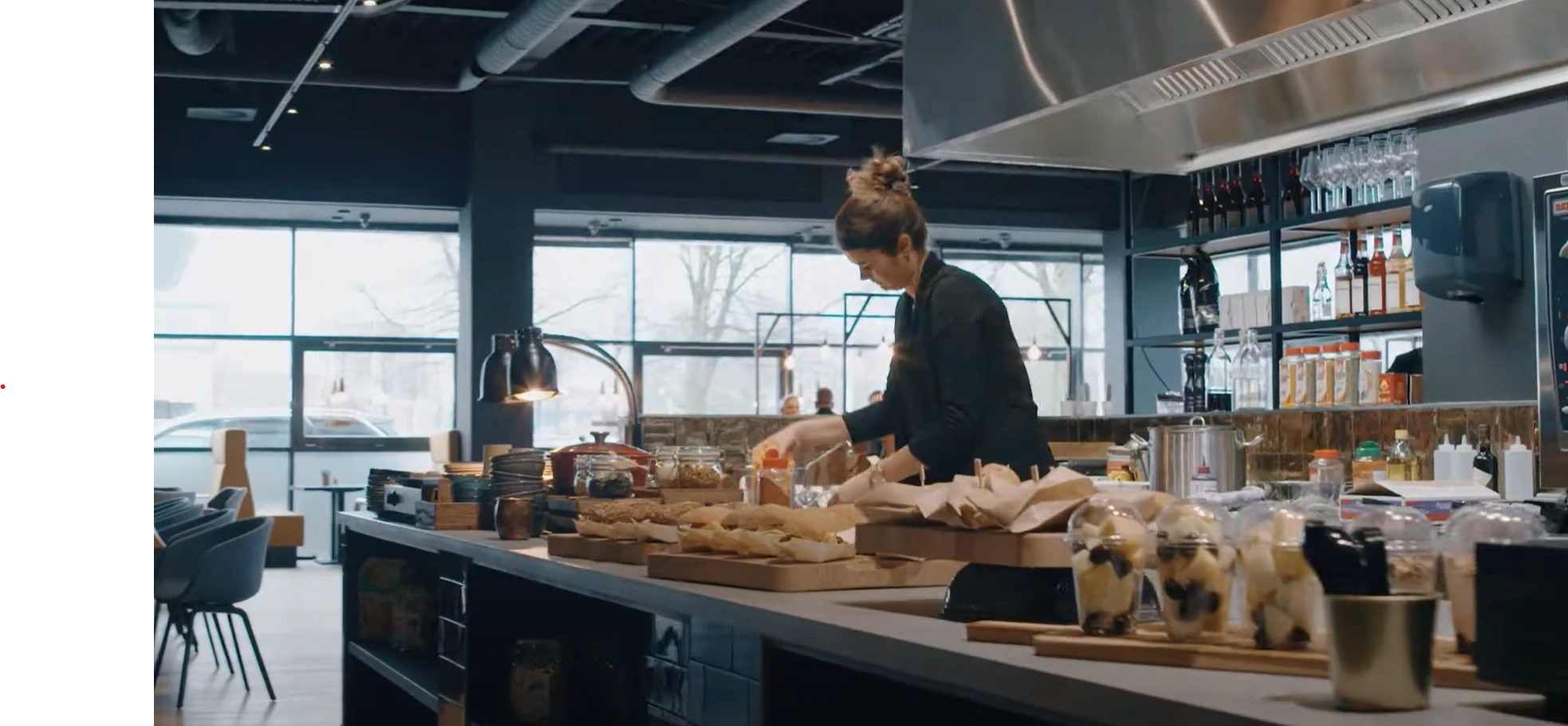 Vrouw legt eten klaar in een moderne keukenomgeving met ramen op de achtergrond.
