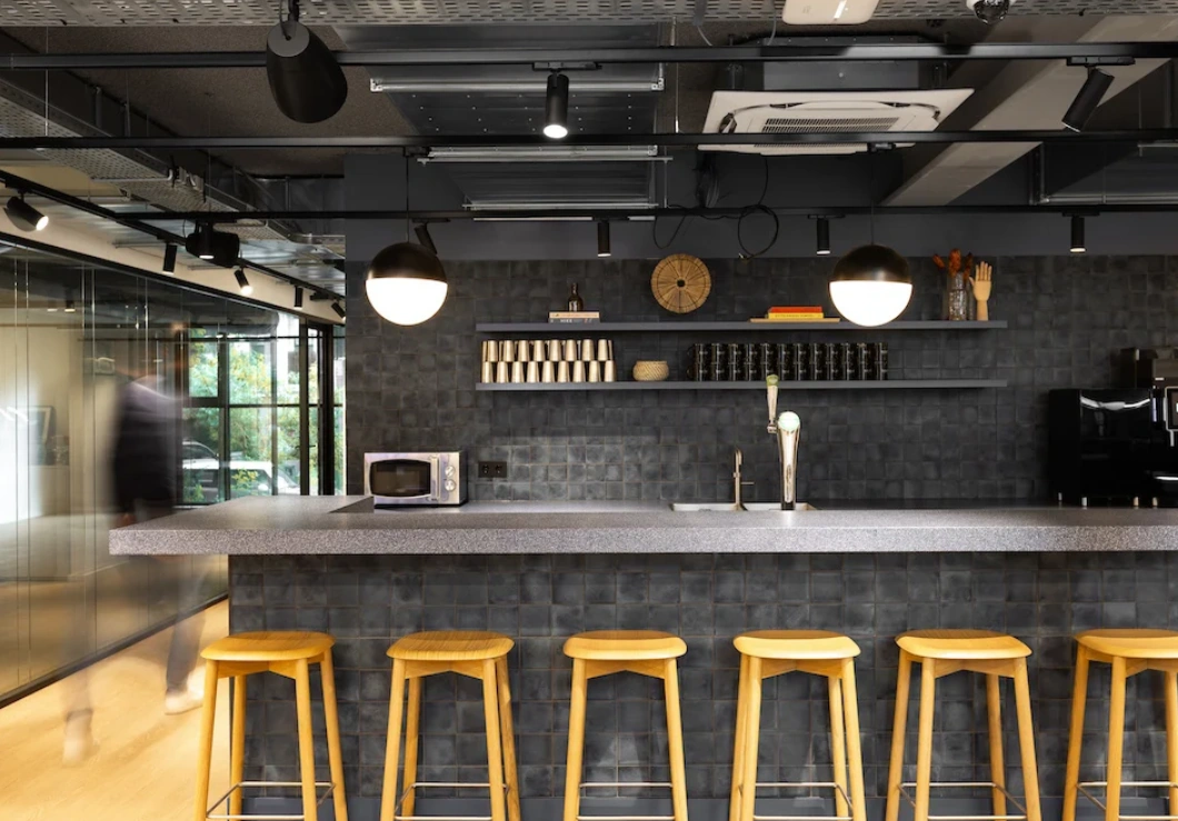 Een moderne kantoorpantry met hoge krukken, een bar, en ingbouwde apparaten en verlichting.