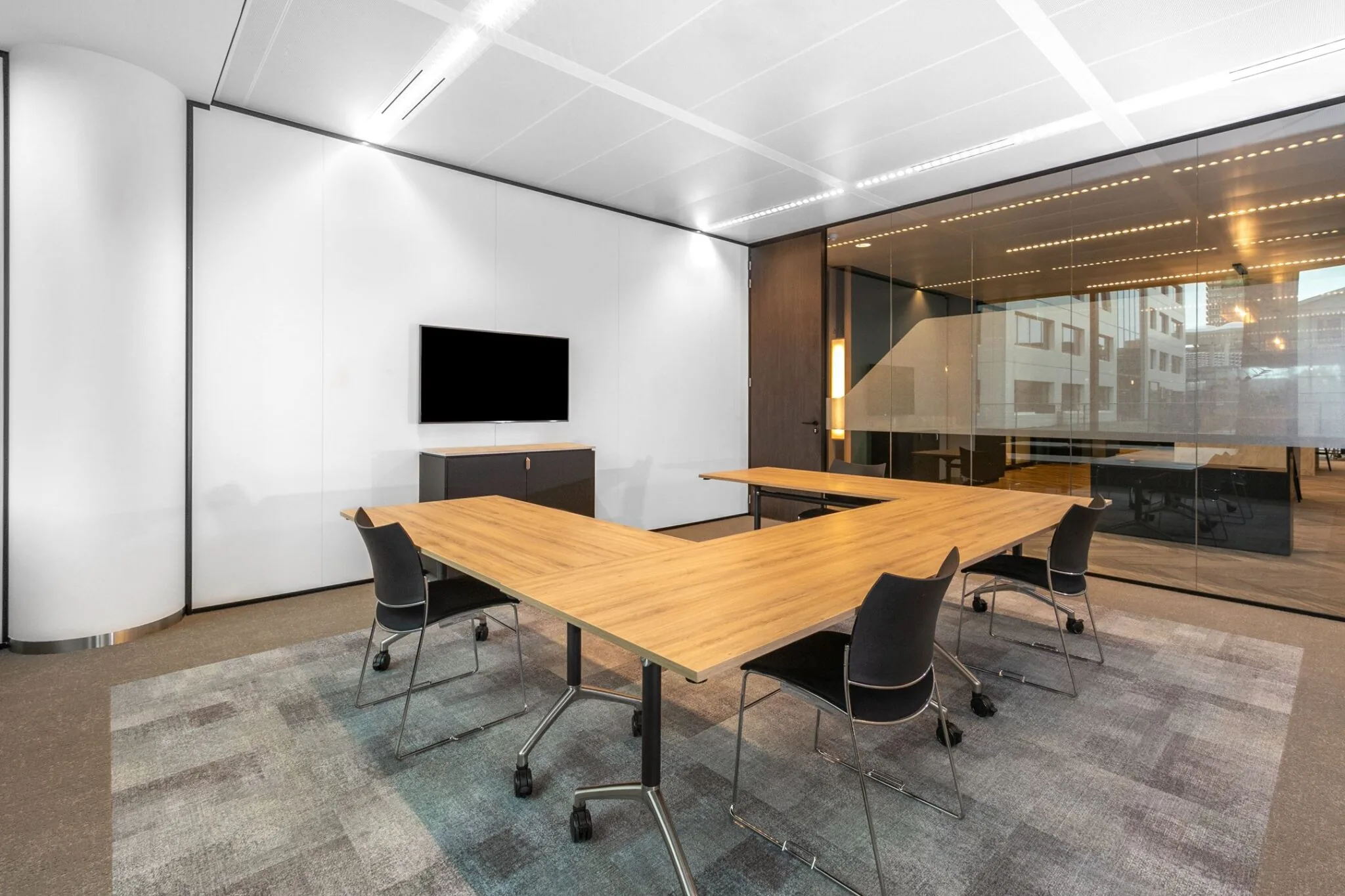 Vergaderruimte met U-vormige houten tafel, zwarte stoelen, een flatscreen en glazen wand aan het Stadsplateau 7.
