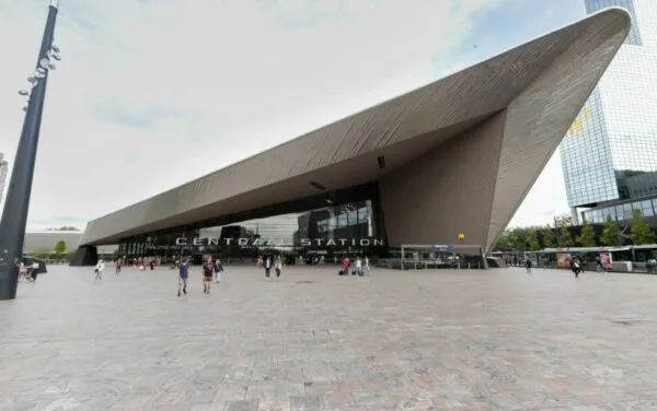 Voorgevel van Rotterdam Centraal Station met het plein en passerende voetgangers op de voorgrond.