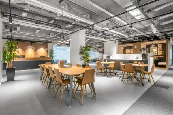 Moderne gemeenschappelijke werkruimte met houten meubels, planten en een open keuken in het kantoorgebouw op Stationsplein 18.