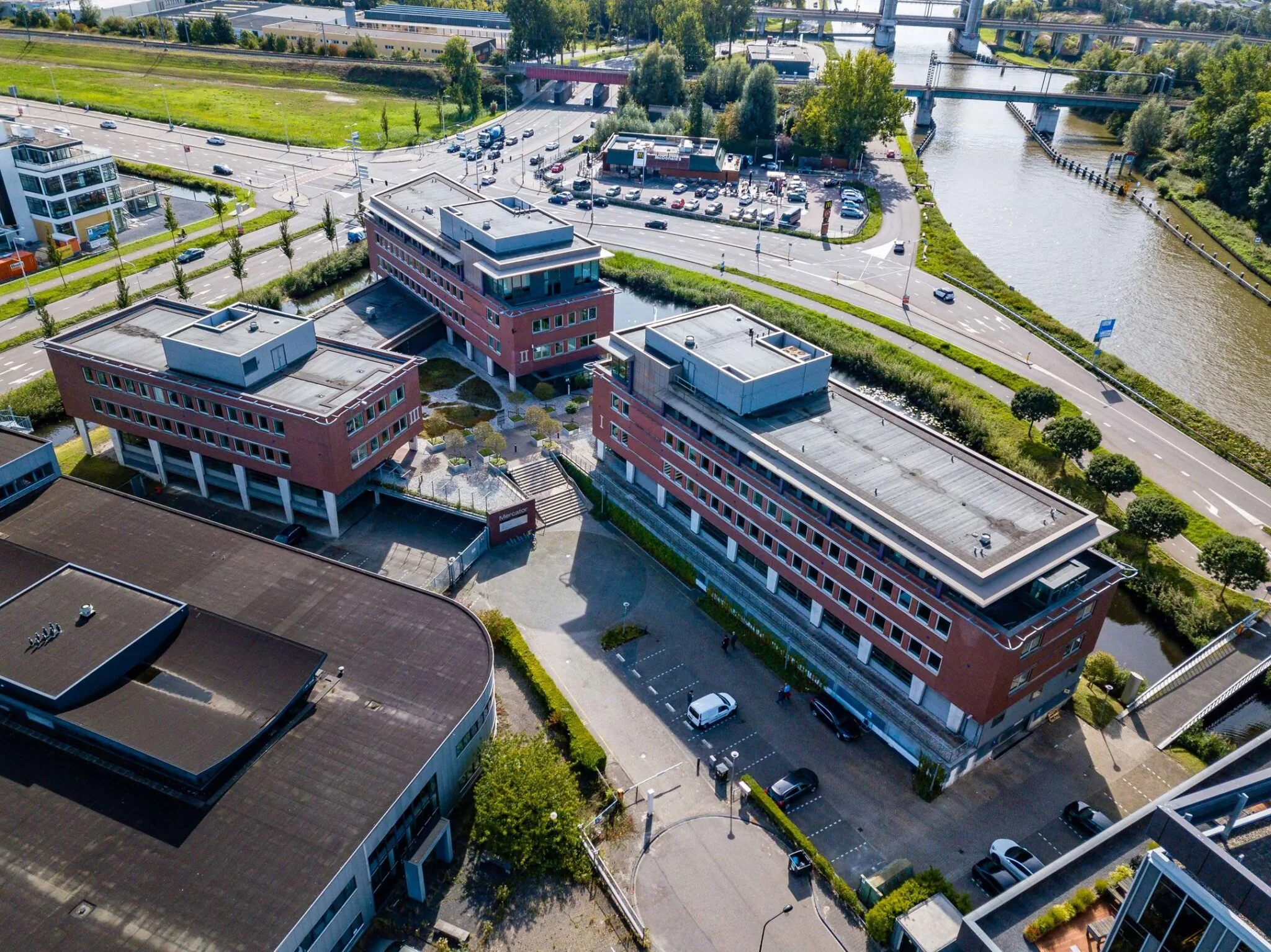 Luchtfoto van het kantoorgebouw aan de Tielweg 30 in Gouda, gelegen langs een waterweg en nabij een druk kruispunt.
