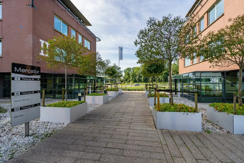 Ingang van het Mercator bedrijfsgebouw aan de Tielweg met moderne beplanting en zicht op gebouwen 26 en 28.