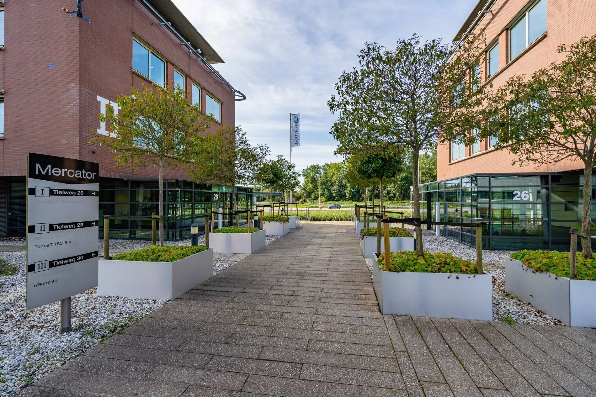 Ingang van het Mercator bedrijfsgebouw aan de Tielweg met moderne beplanting en zicht op gebouwen 26 en 28.