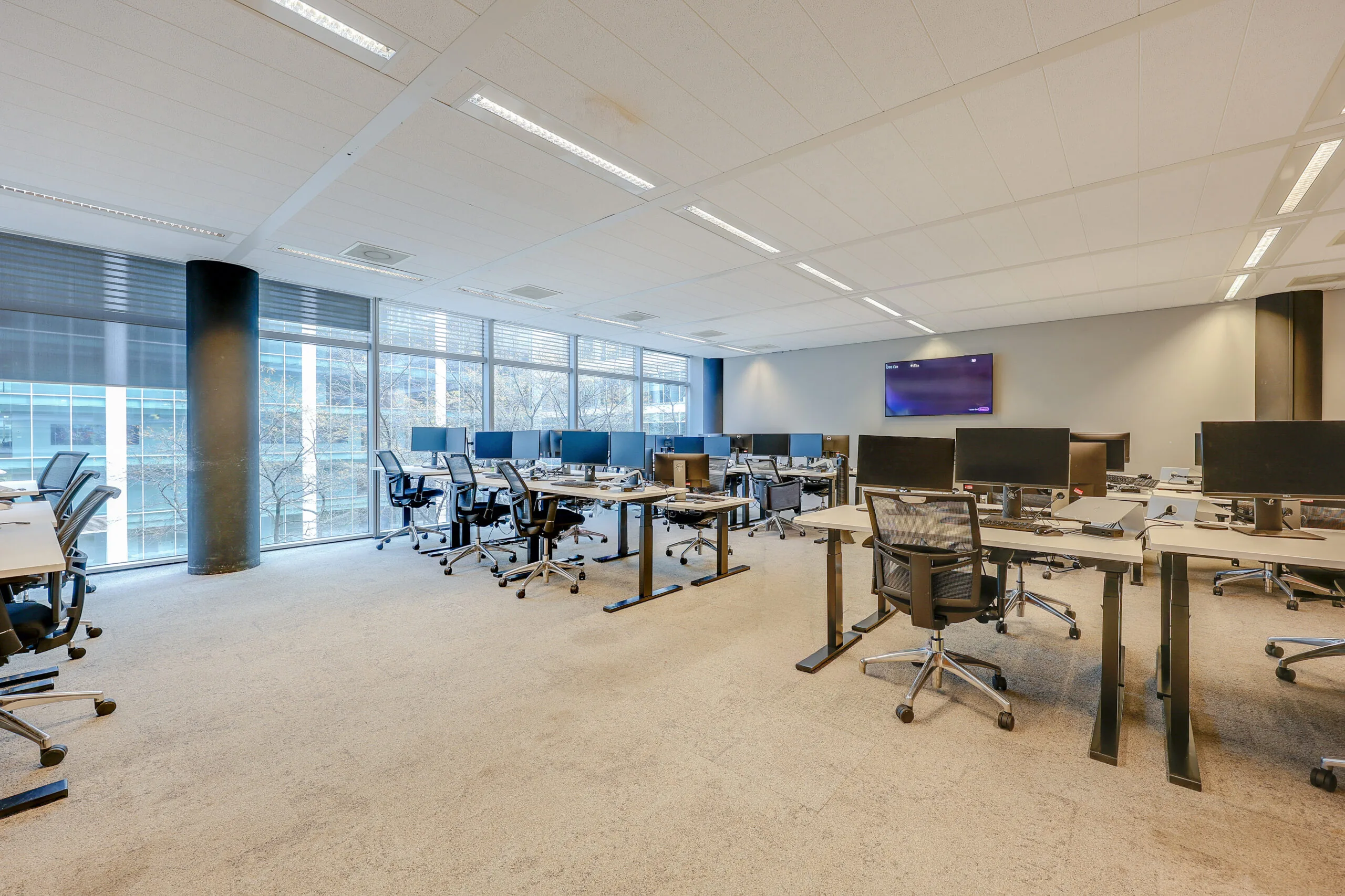 Een modern, ruim kantoor met bureaus, stoelen en meerdere computerschermen bij Tribes Amsterdam SOM.