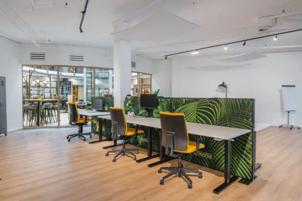 Moderne kantoorruimte met bureaus en stoelen, gescheiden door groene plantenafbeeldingen.