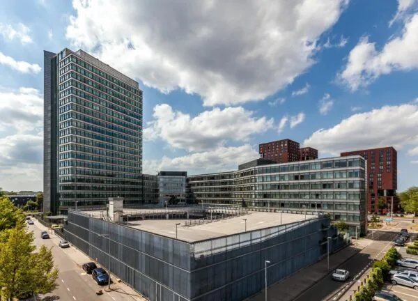 Modern kantoorgebouw en parkeergarage aan de Vliegend Hertlaan 21 in Utrecht, met omliggende hoogbouw onder een deels bewolkte hemel.