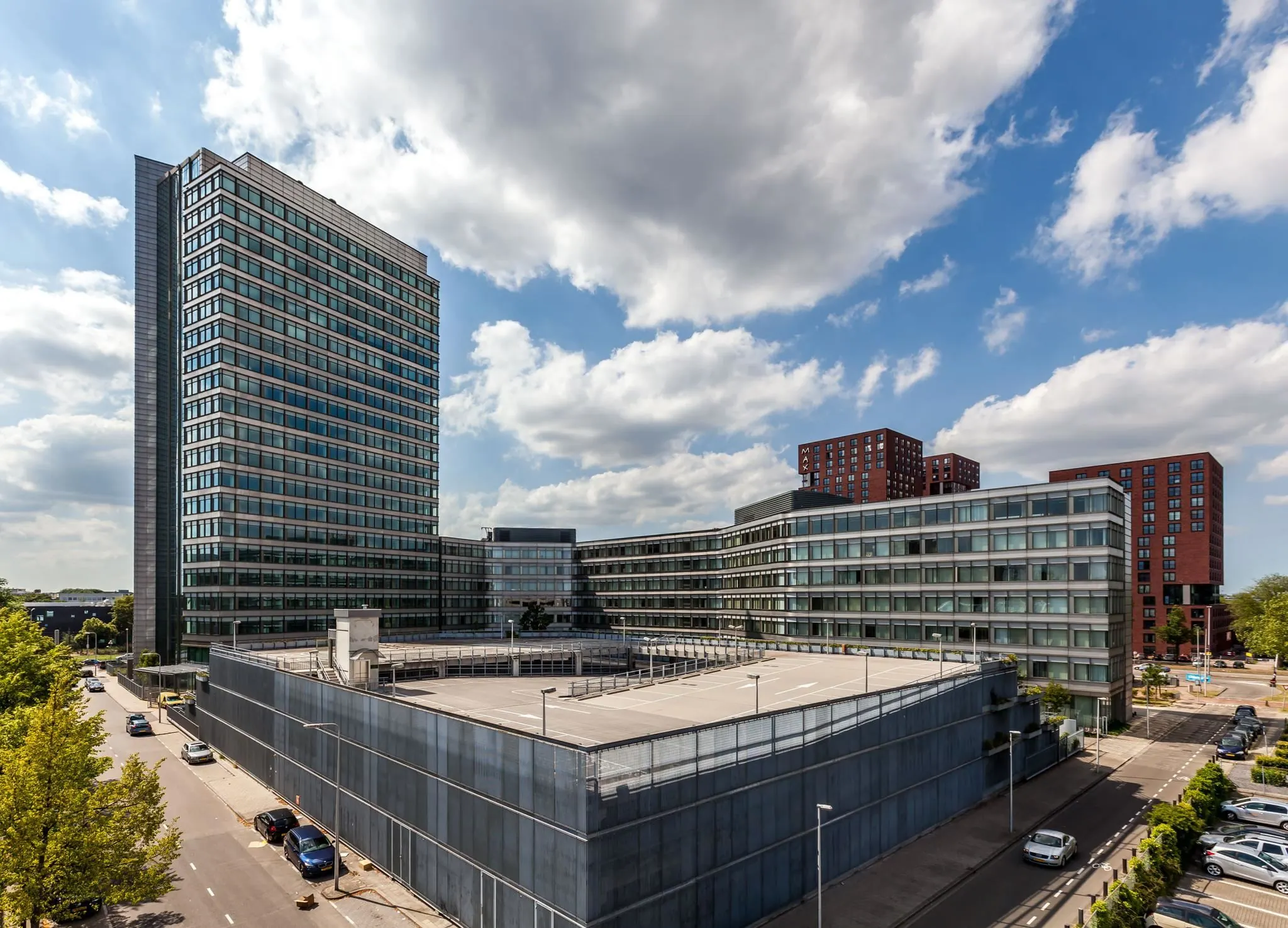Modern kantoorgebouw en parkeergarage aan de Vliegend Hertlaan 21 in Utrecht, met omliggende hoogbouw onder een deels bewolkte hemel.