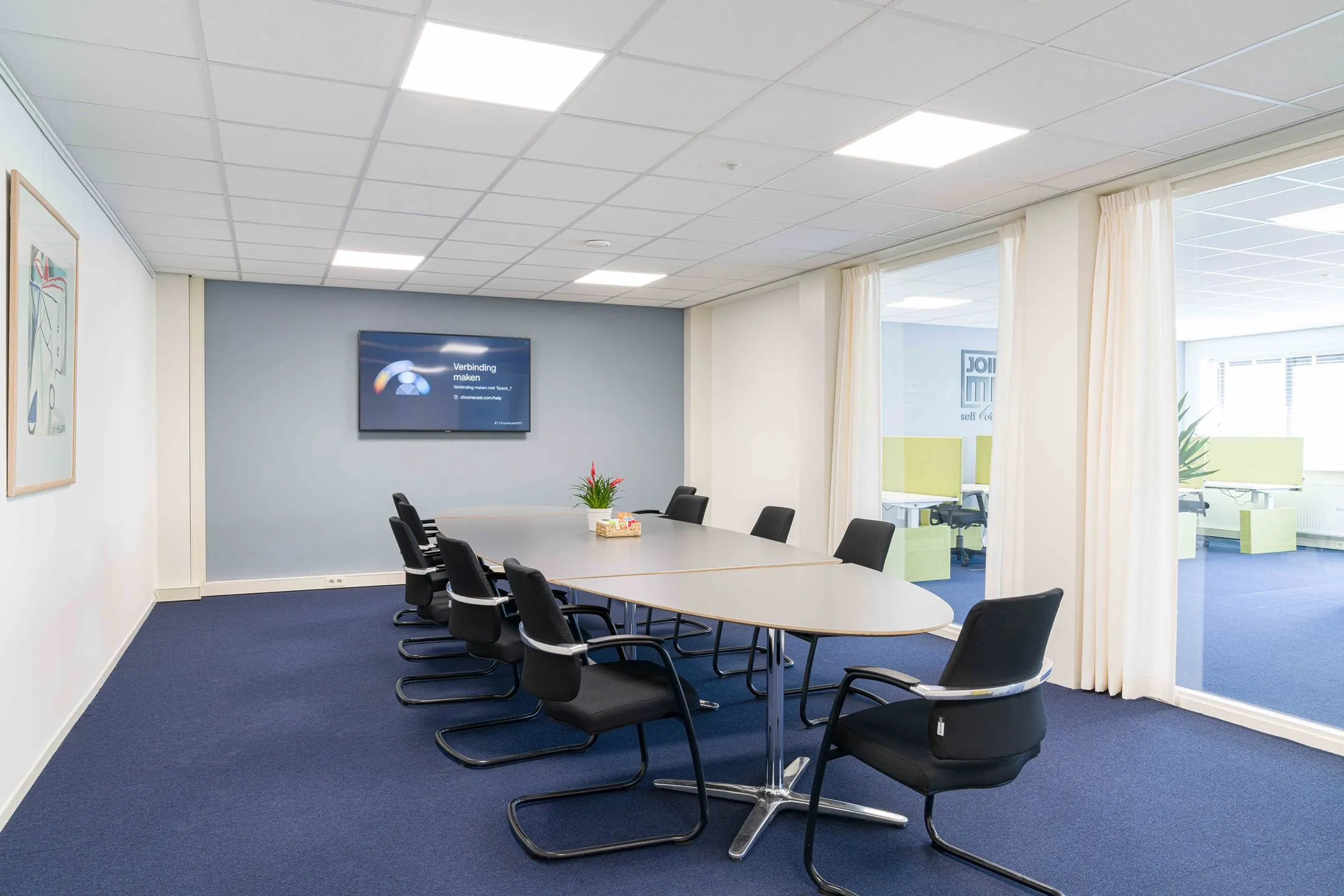 Vergaderruimte met ovale tafel, acht stoelen, presentatiescherm en zicht op aangrenzend kantoorgedeelte in het pand aan de Waarderweg 33.