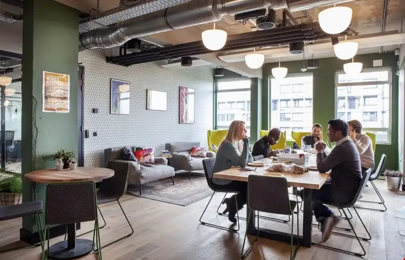 Mensen zitten aan een tafel in een modern ingerichte kantoorruimte aan de Weesperstraat 61-105.