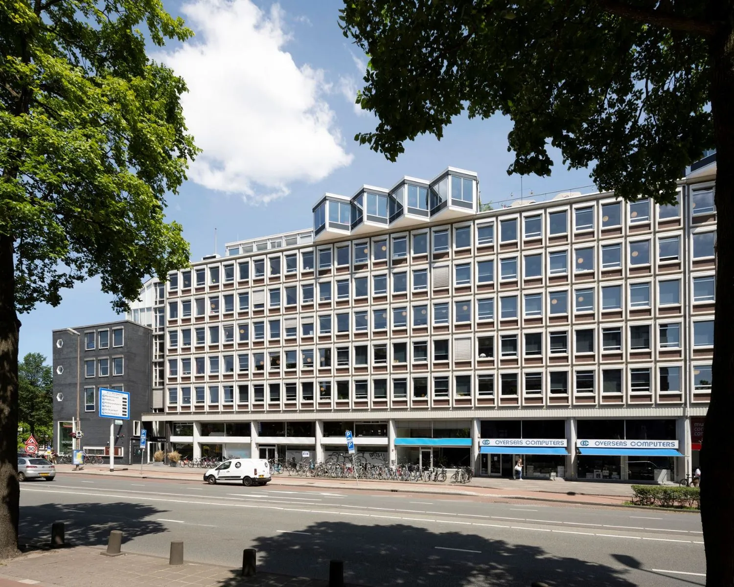 Straatbeeld van het kantoorgebouw aan de Weesperstraat 61-105 in Amsterdam, met winkels en fietsenstalling op de begane grond.