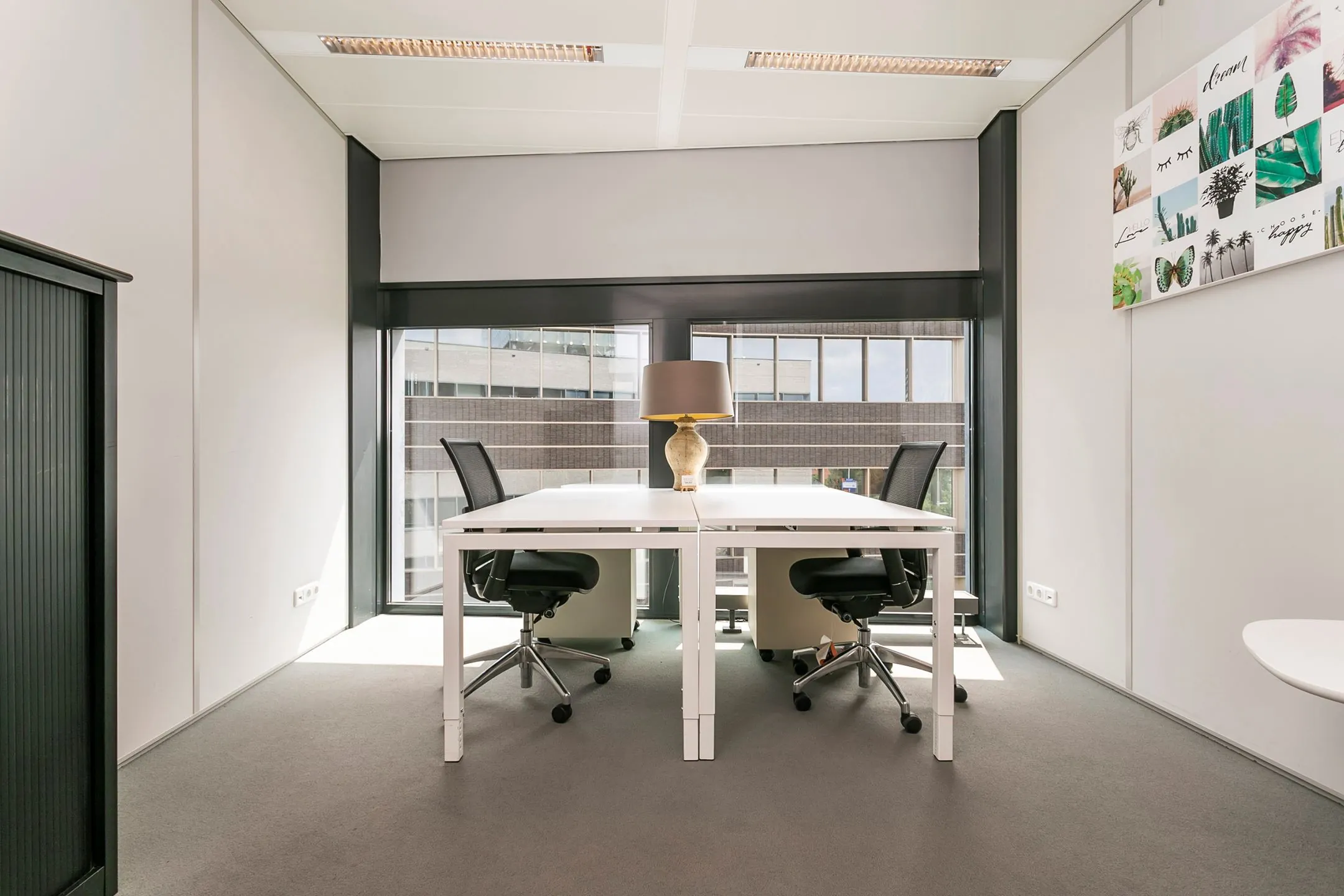 Modern ingerichte kantoorruimte aan het Wim Duisenbergplantsoen met twee bureaus, bureaustoelen en een tafellamp bij grote ramen.