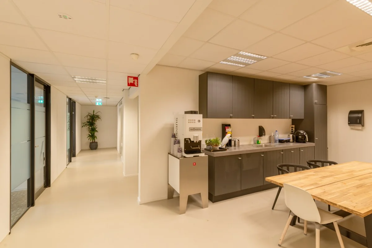 Bedrijfskeuken met koffieautomaat, houten tafel en moderne kasten in een kantoor aan de Atoomweg.