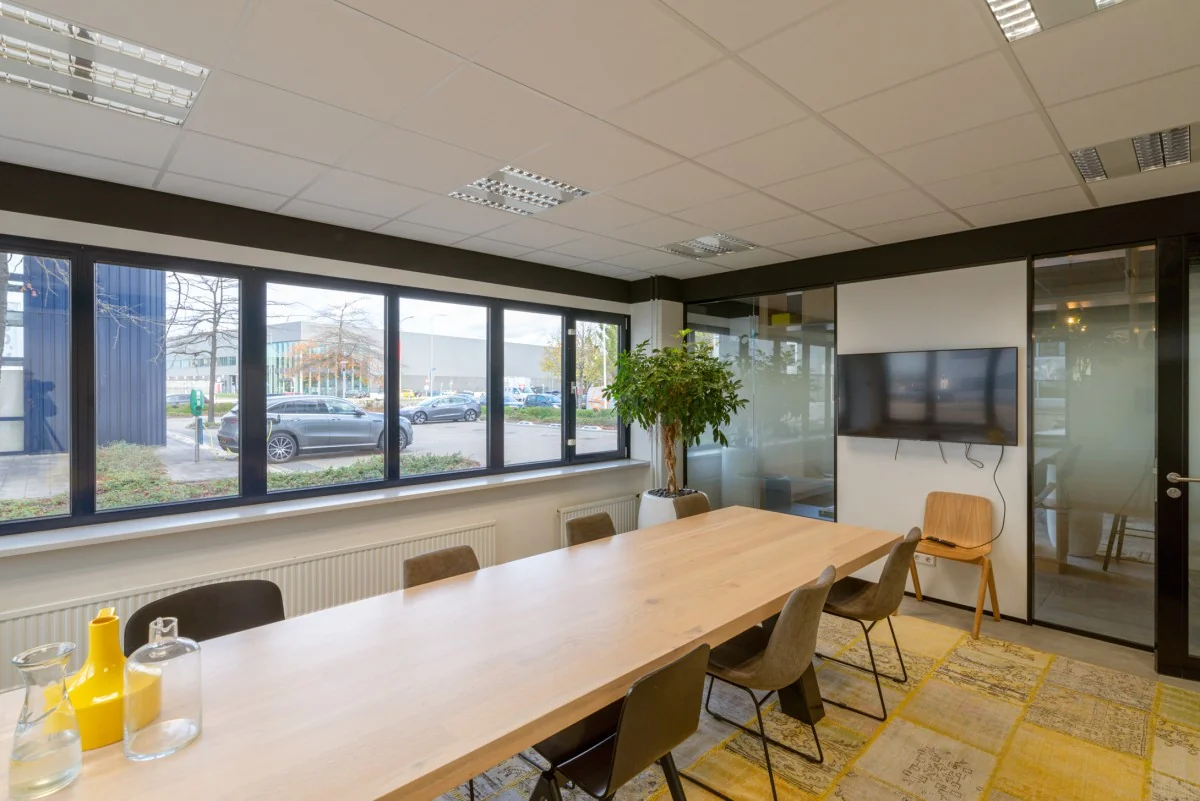 Vergaderruimte in een modern kantoorpand aan de Atoomweg met een lange houten tafel, stoelen, grote ramen en een flatscreen aan de muur.