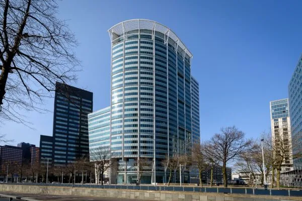 Modern kantoorgebouw Blaak 555 in Rotterdam met glazen gevel, omringd door andere hoogbouw en kale bomen in de voorgrond.