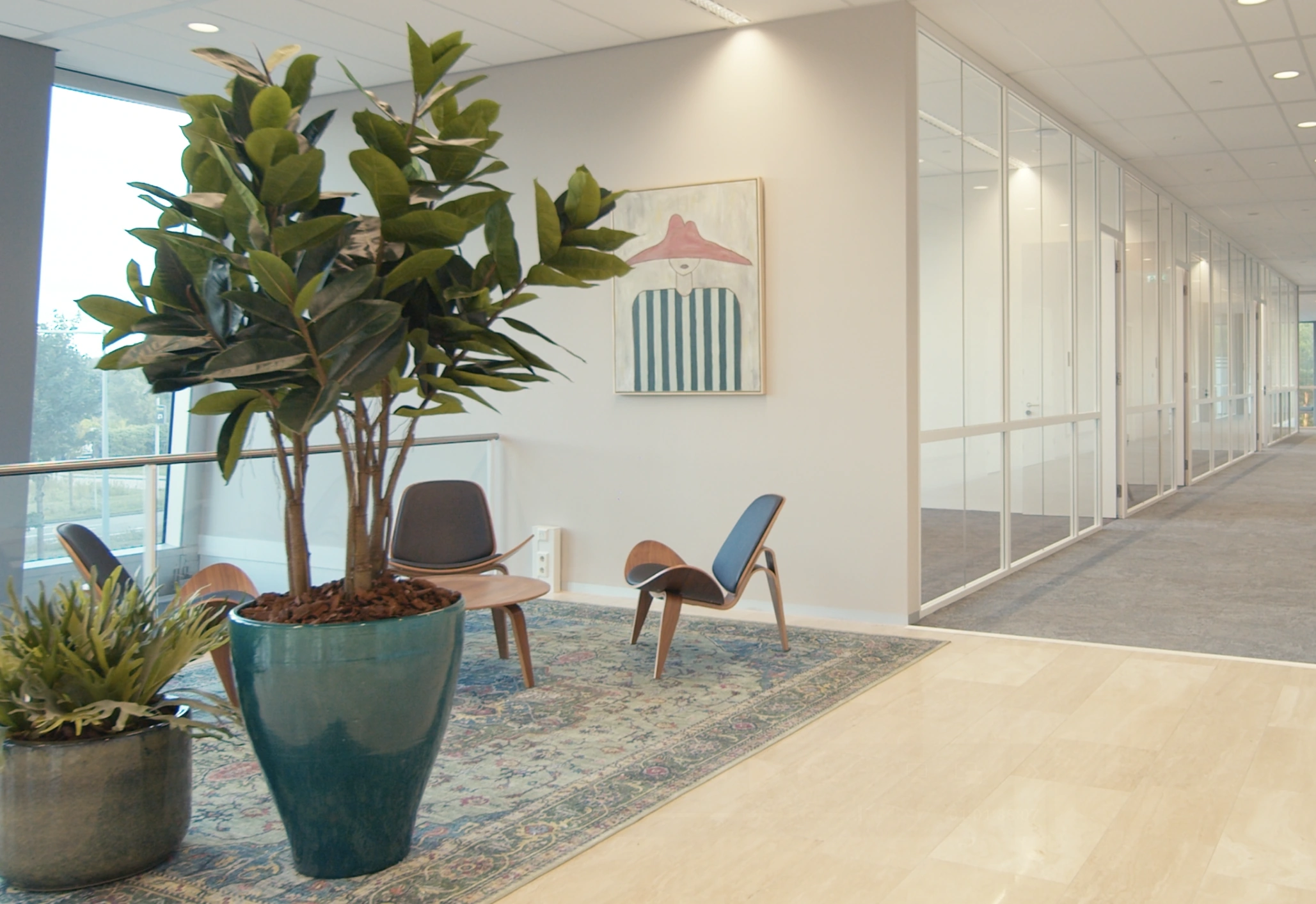 Moderne wachtruimte in een kantoor met planten, designstoelen en kunstwerk aan de muur.
