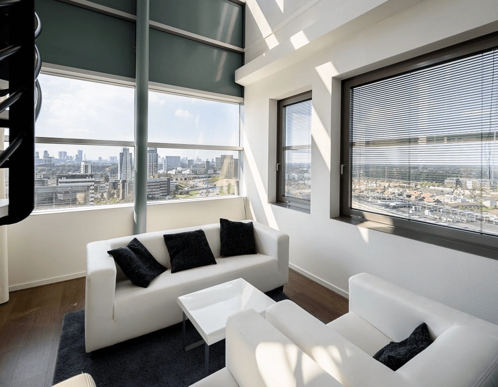Modern ingericht kantoor met witte banken en uitzicht op de skyline van een stad door grote ramen.