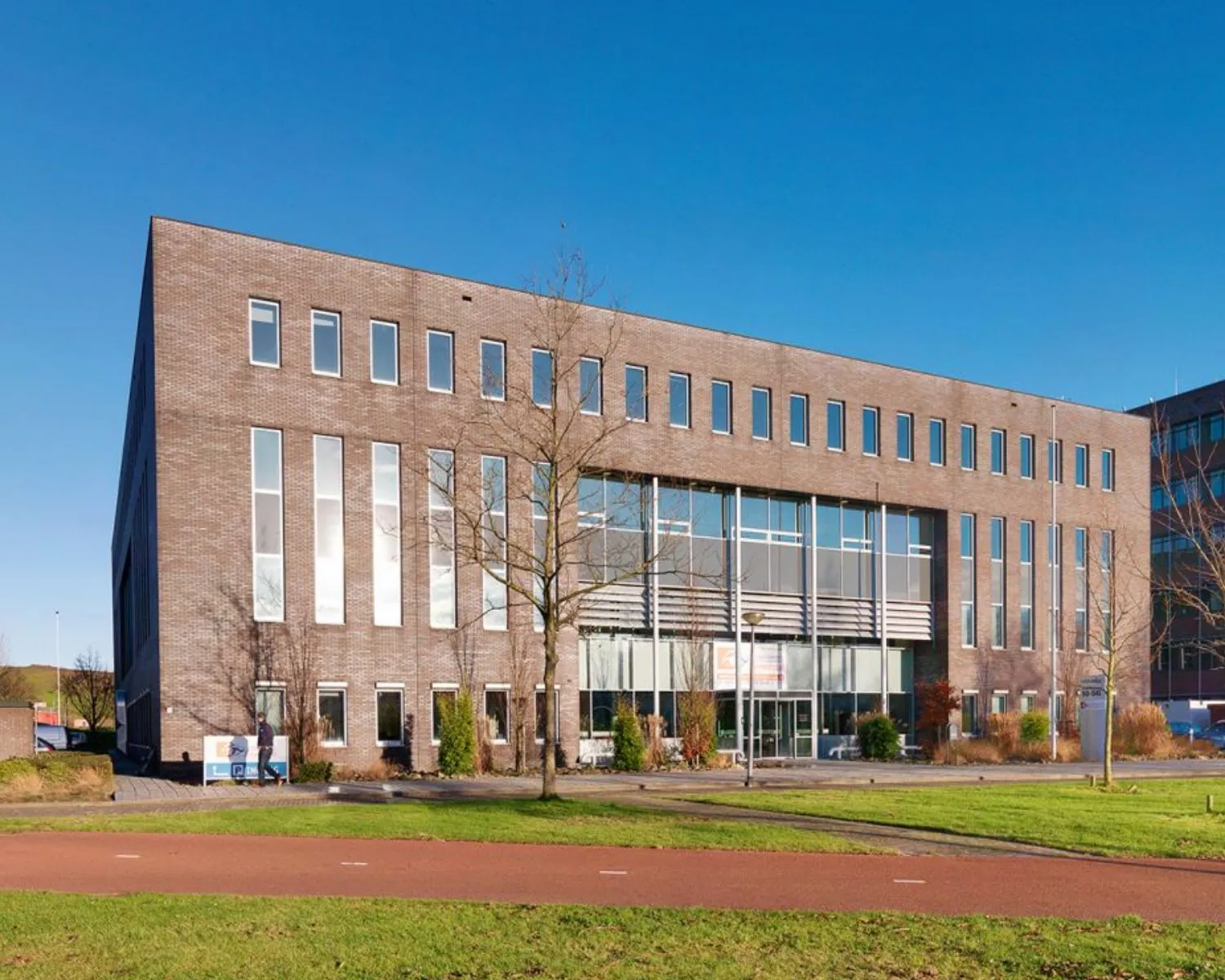 Modern kantoorgebouw met een bakstenen gevel en grote ramen op een zonnige dag.