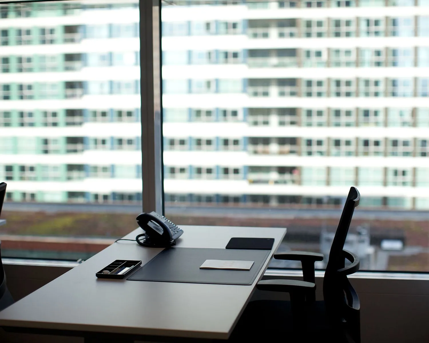 Modern kantoor met een leeg bureau, telefoontoestel en uitzicht op een hoog gebouw met glazen ramen.