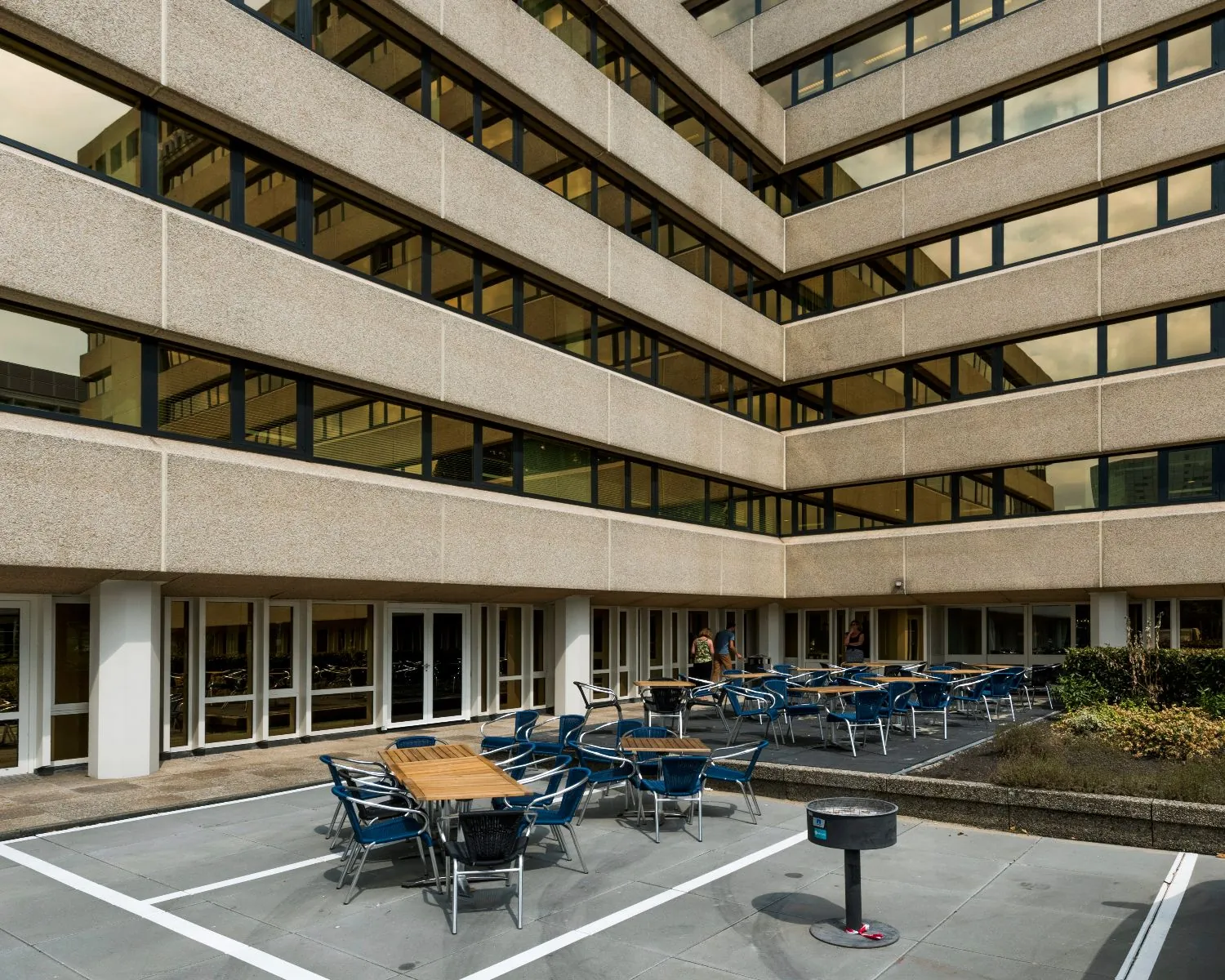 Buitenruimte met tafels en stoelen bij een modern kantoorgebouw met grote ramen.