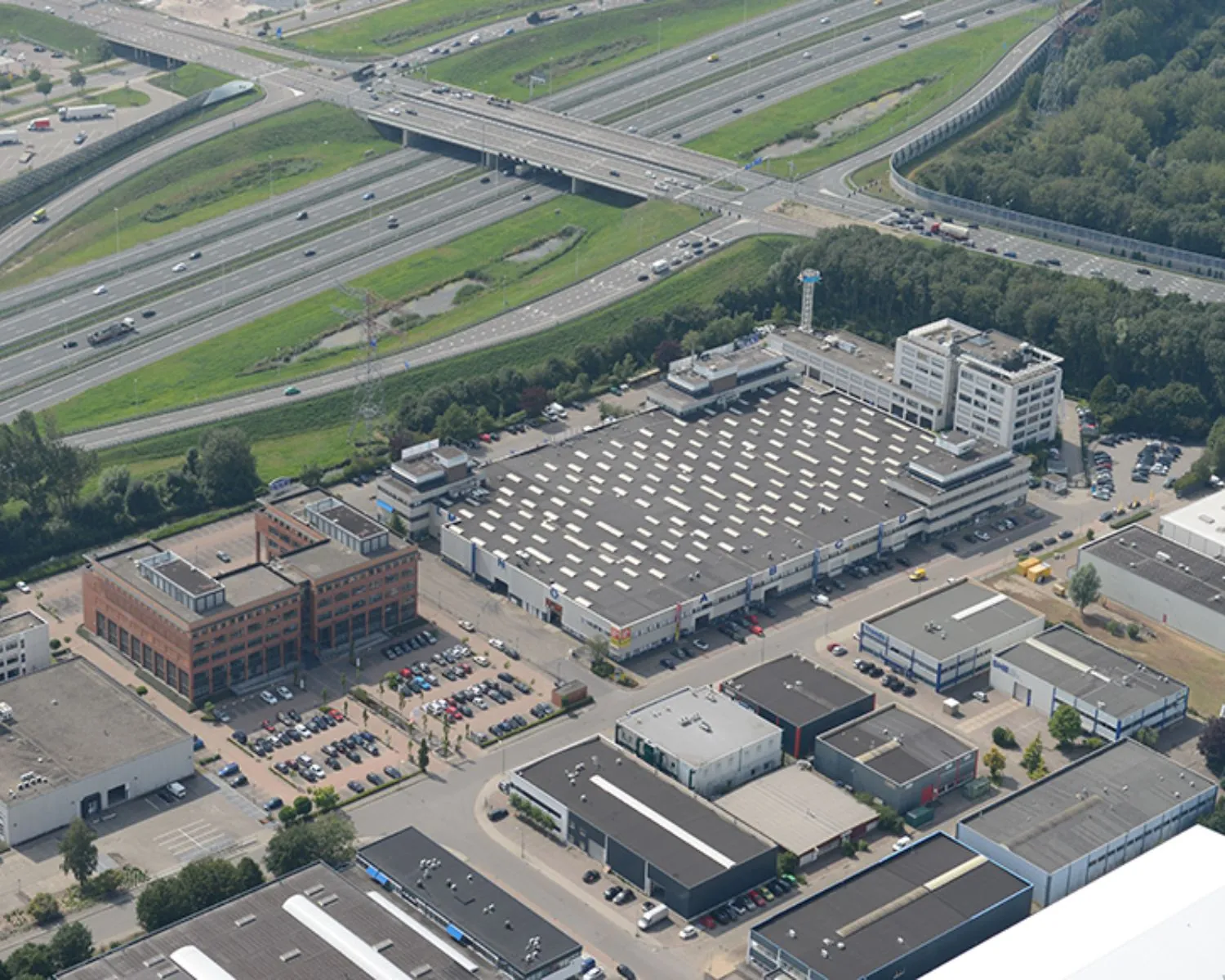 Luchtfoto van een bedrijventerrein nabij een knooppunt van snelwegen met kantoren, magazijnen en parkeerplaatsen.