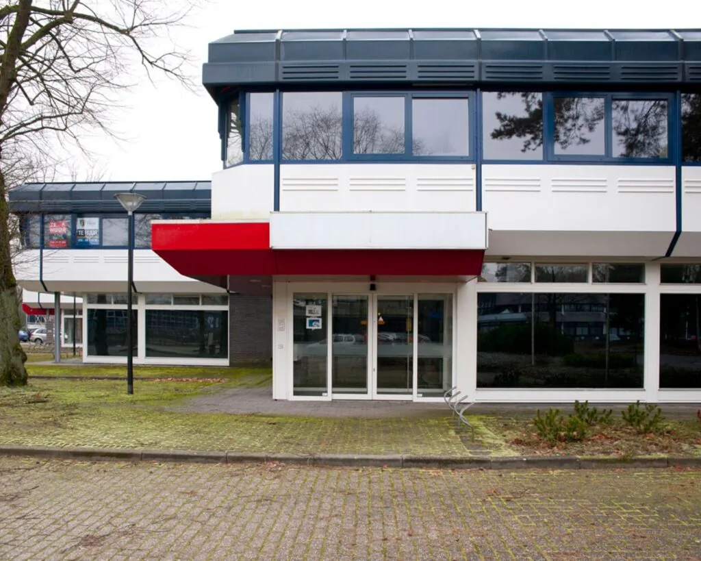 Vooraanzicht van een leegstaand kantoorpand met rood-witte luifel en ‘Te Huur’-borden in de ramen.