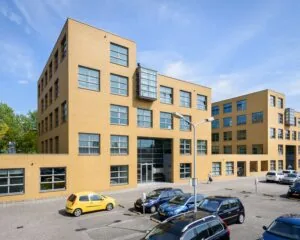 Modern kantoorgebouw met een gele bakstenen gevel en meerdere geparkeerde auto’s op de voorgrond.