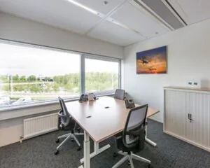 Kleine vergaderruimte met vier stoelen, een vergadertafel en een groot raam met uitzicht op groen.