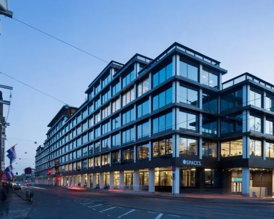Modern kantoorgebouw van Spaces met glazen gevel aan een stadsstraat bij schemering.