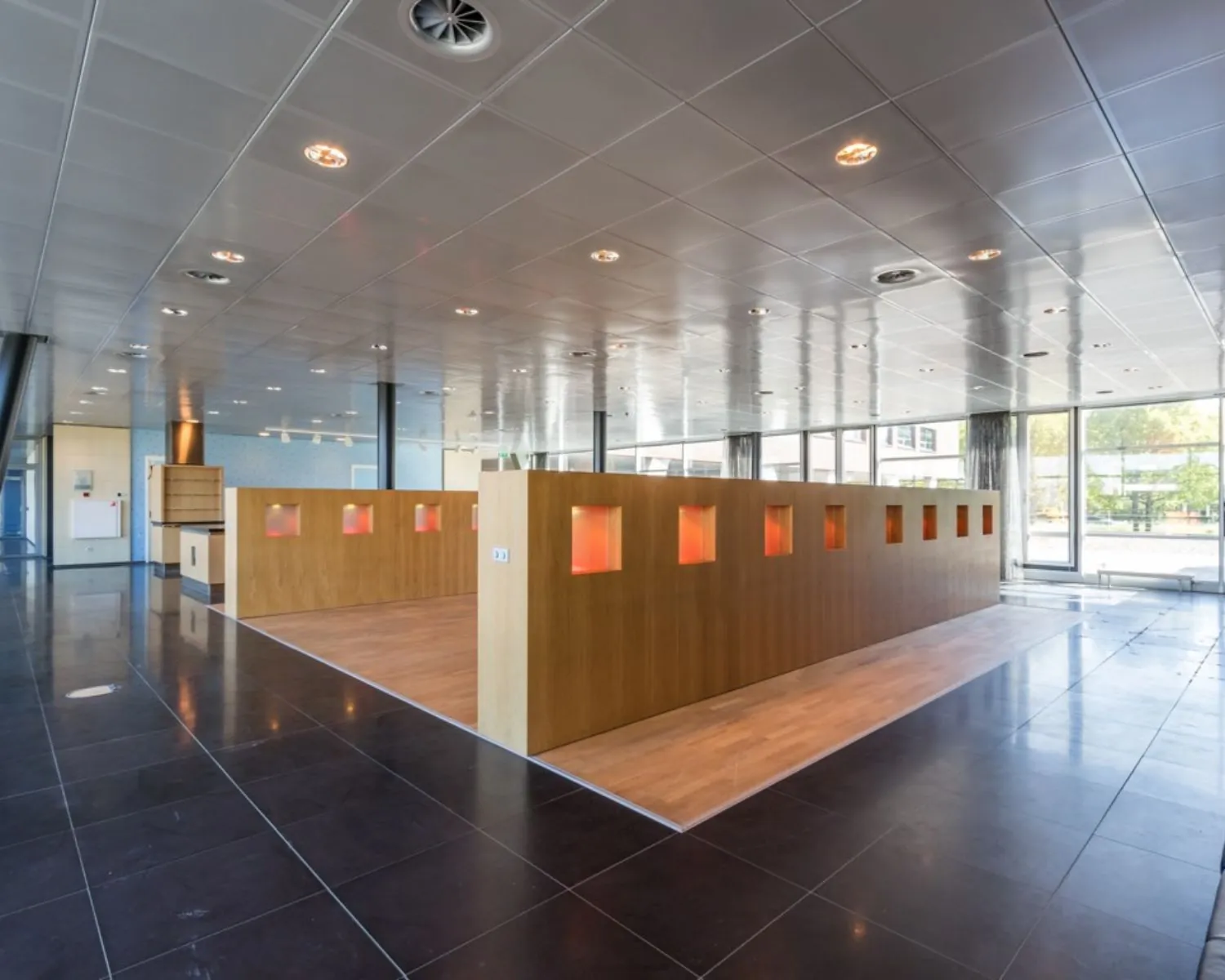 Moderne, open kantoorruimte met houten scheidingswand met verlichte nissen en grote ramen.