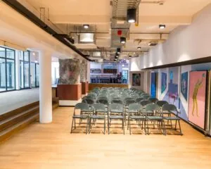 Opgestelde rijen met klapstoelen in een moderne, industriële evenementenruimte met kunst aan de muur.