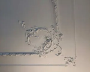 Wit plafond met sierlijke, barokke stucdecoratie in een hoekpatroon.