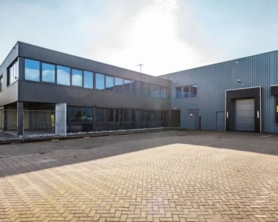Grijze, moderne bedrijfsloods met grote ramen en rolluikdeur op een ruim, betegeld terrein.