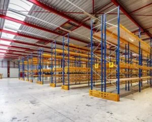 Lege magazijnhal met hoge, metalen opslagstellingen en betonnen vloer.